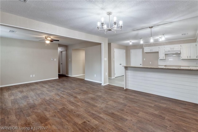 unfurnished living room featuring ceiling fan with notable chandelier, dark wood-type flooring, and a textured ceiling