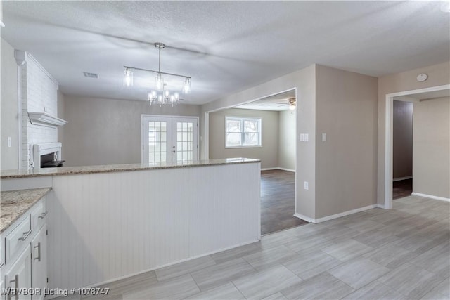 kitchen with french doors, decorative light fixtures, a textured ceiling, a large fireplace, and white cabinets