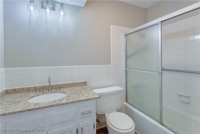 full bathroom with vanity, tile walls, shower / bath combination with glass door, and toilet