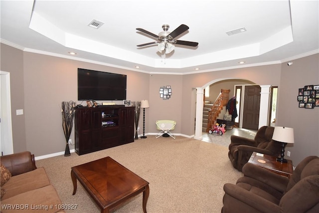carpeted living area with ornate columns, a tray ceiling, arched walkways, a ceiling fan, and ornamental molding