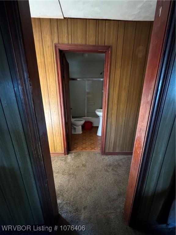 hallway with carpet flooring and wooden walls