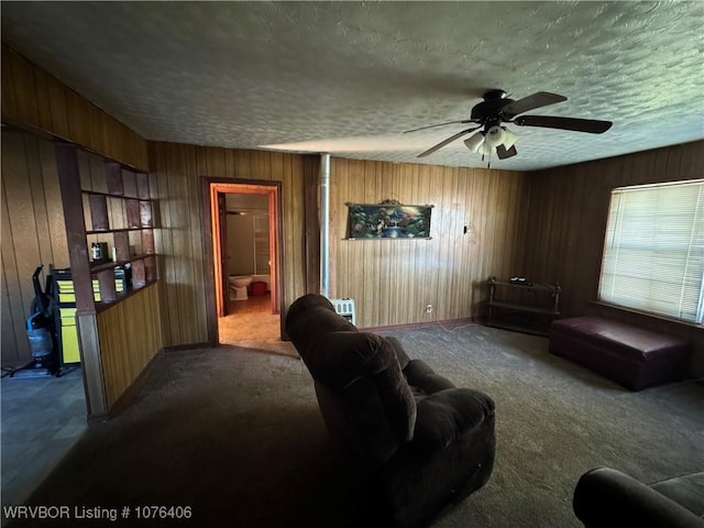 carpeted living room featuring ceiling fan, a textured ceiling, and wooden walls