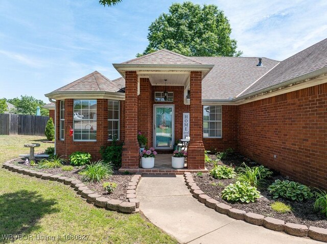 entrance to property with fence, brick siding, and roof with shingles