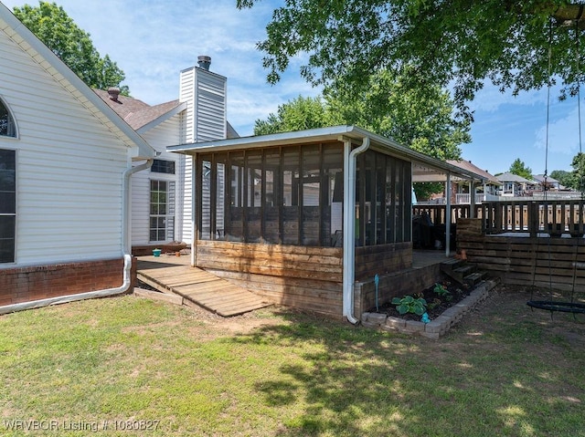 rear view of property with a chimney, a sunroom, and a yard
