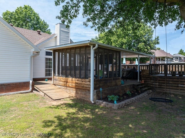 back of house with a chimney, a sunroom, a yard, a wooden deck, and roof with shingles