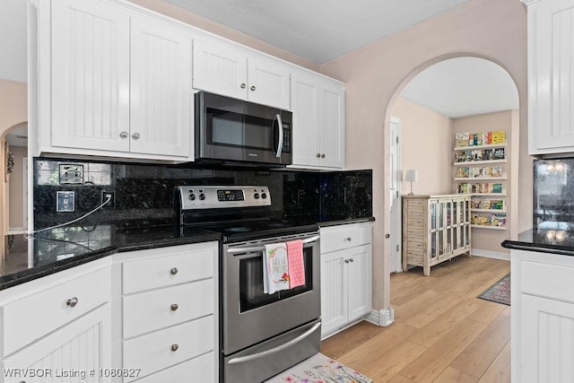 kitchen featuring appliances with stainless steel finishes, arched walkways, white cabinets, light wood-style flooring, and decorative backsplash