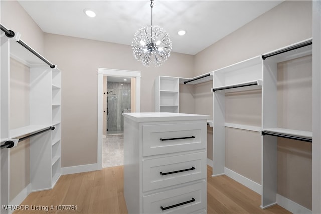 spacious closet with light wood-type flooring and an inviting chandelier