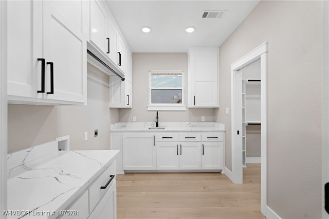 kitchen featuring white cabinetry, sink, light stone countertops, and light wood-type flooring