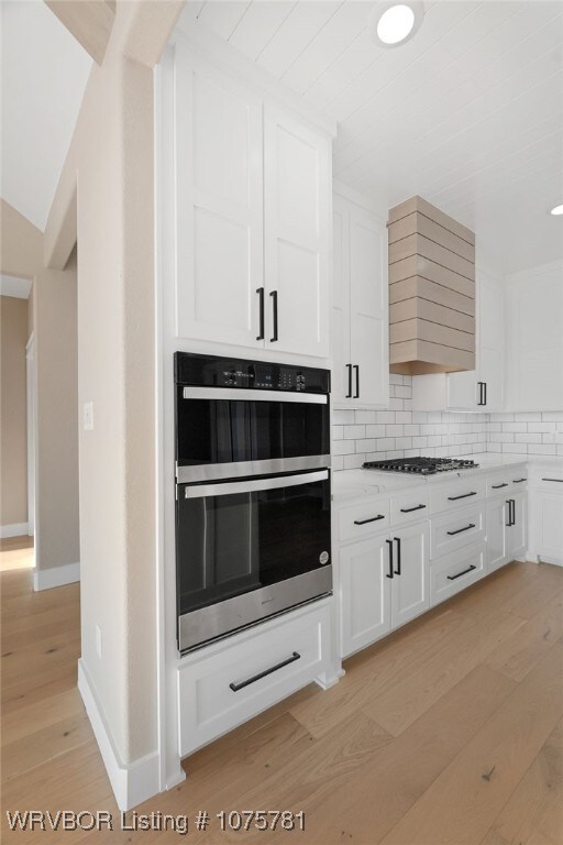 kitchen featuring premium range hood, backsplash, white cabinetry, and stainless steel appliances