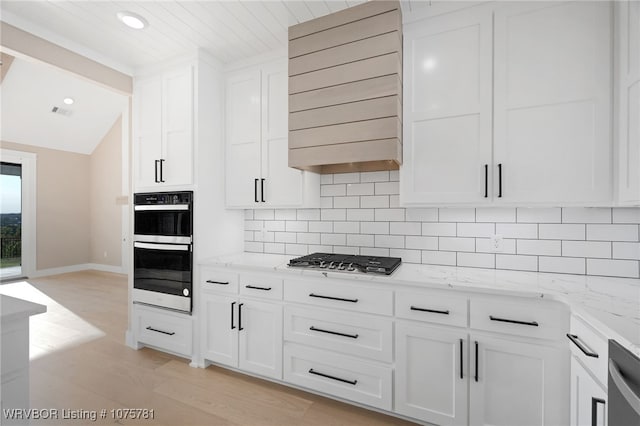 kitchen with white cabinetry, light stone countertops, premium range hood, backsplash, and appliances with stainless steel finishes