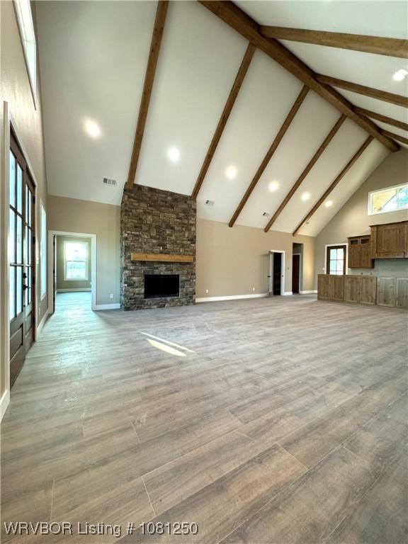 4457 Radio Tower Rd, Van Buren, AR 72956 - unfurnished living room featuring high vaulted ceiling, beamed ceiling, a stone fireplace, light wood-style floors, and baseboards