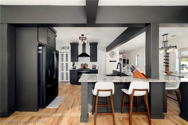 kitchen featuring light stone countertops, sink, wall chimney range hood, a kitchen bar, and black appliances