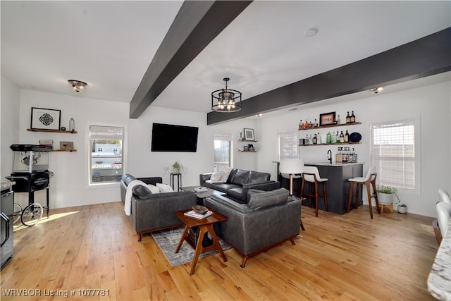 living room featuring beam ceiling, indoor wet bar, light wood-type flooring, and an inviting chandelier