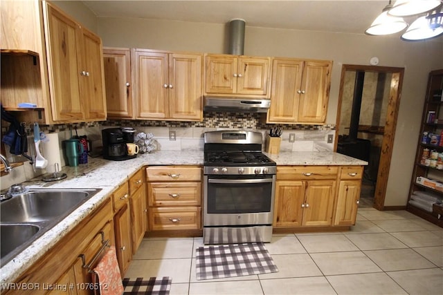 kitchen featuring light tile patterned floors, decorative backsplash, stainless steel gas stove, a sink, and under cabinet range hood