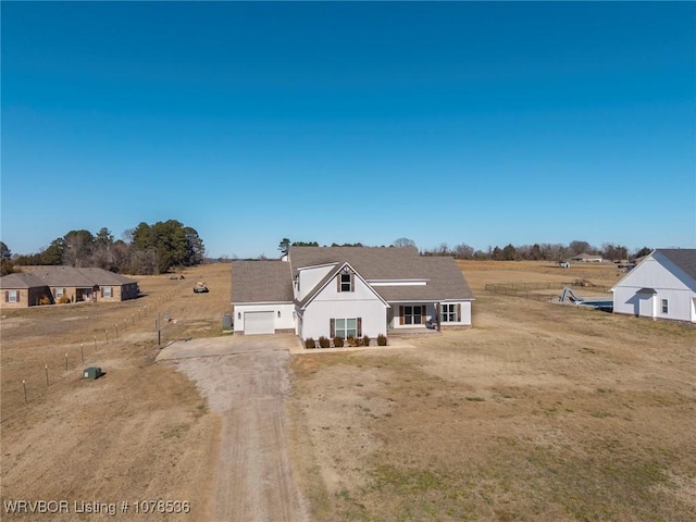 view of front of property with covered porch, a front yard, a garage, and a rural view