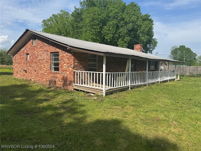 rear view of house with a chimney, fence, a lawn, brick siding, and metal roof