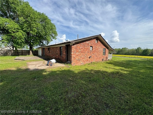 view of side of property featuring brick siding, fence, and a yard