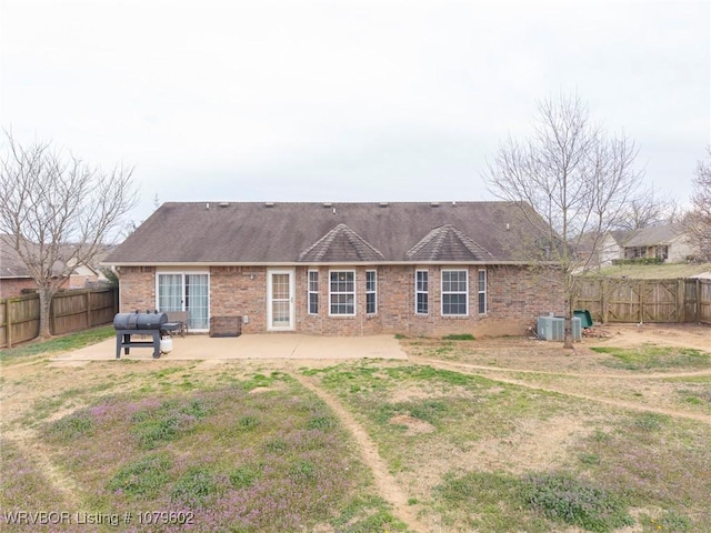 rear view of house with cooling unit, a patio, brick siding, and a fenced backyard