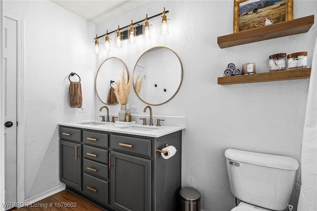 bathroom with double vanity, toilet, wood finished floors, and a sink