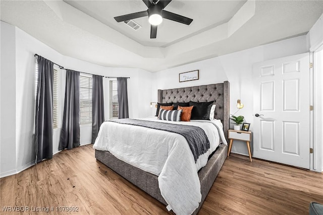 bedroom featuring a ceiling fan, a tray ceiling, wood finished floors, and visible vents