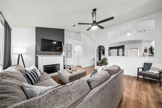 living room featuring a brick fireplace, wood finished floors, arched walkways, and ceiling fan