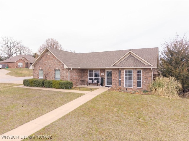 single story home featuring a front yard, brick siding, and roof with shingles