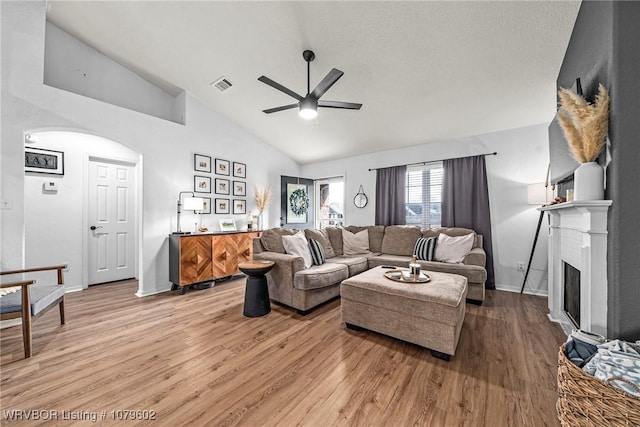 living area with visible vents, light wood-style flooring, a ceiling fan, arched walkways, and a fireplace