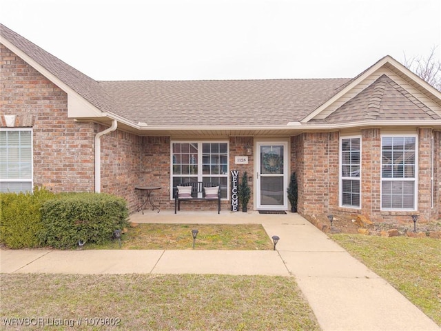 view of front facade with a patio area, brick siding, and roof with shingles