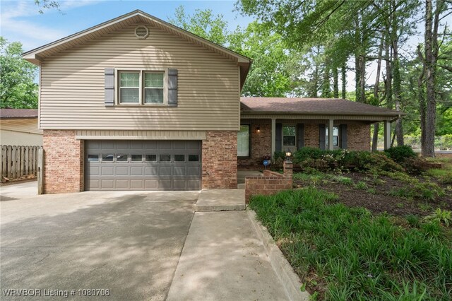 tri-level home with fence, an attached garage, concrete driveway, and brick siding