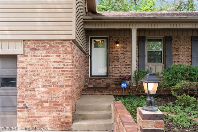 entrance to property featuring a porch and brick siding