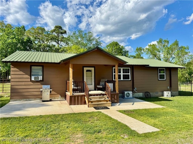 rear view of house with fence, covered porch, cooling unit, metal roof, and a yard
