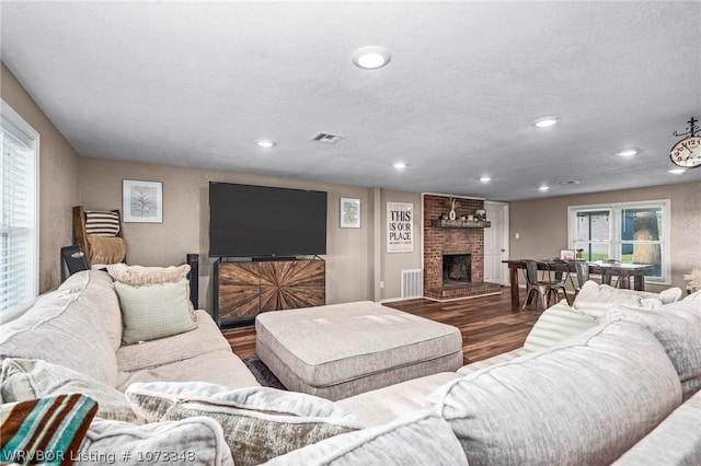 living room with hardwood / wood-style floors, a textured ceiling, and a brick fireplace