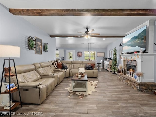 living area featuring beamed ceiling, a ceiling fan, wood finished floors, and a stone fireplace