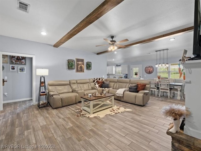 living area featuring light wood-style flooring, beam ceiling, baseboards, visible vents, and a ceiling fan
