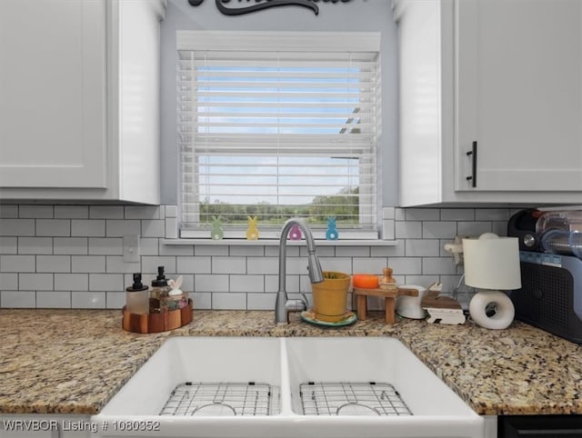 kitchen with light stone counters, decorative backsplash, white cabinetry, and a sink
