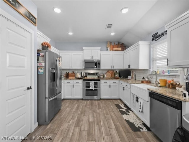 kitchen featuring white cabinets, stainless steel appliances, tasteful backsplash, light wood-type flooring, and light stone counters
