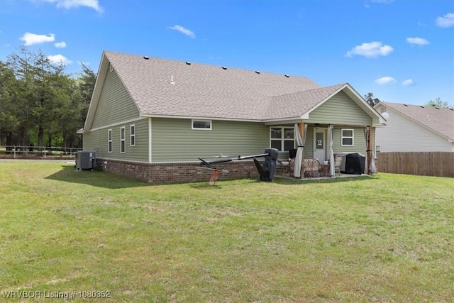 rear view of house with a yard, a shingled roof, and fence