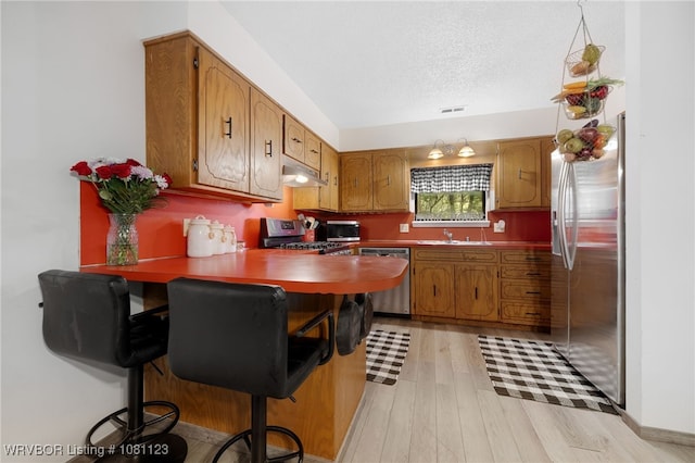 175 Sulphur City Rd, Fayetteville, AR 72701 - kitchen with stainless steel appliances, under cabinet range hood, light wood-style floors, brown cabinetry, and a textured ceiling