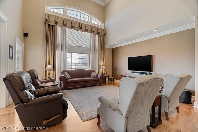 living room with ornamental molding, a healthy amount of sunlight, light hardwood / wood-style flooring, and a towering ceiling