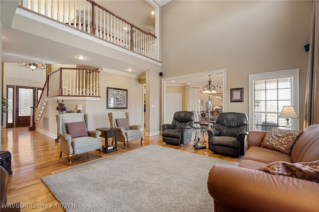 living room with ornamental molding, a chandelier, a high ceiling, and light wood-type flooring