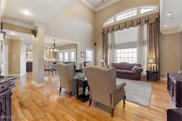 living room featuring crown molding, a healthy amount of sunlight, an inviting chandelier, and light hardwood / wood-style floors