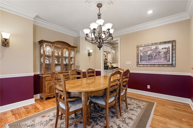 dining space with ornamental molding, an inviting chandelier, and light wood-type flooring