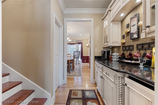 interior space featuring a notable chandelier, ornamental molding, light hardwood / wood-style floors, and dark stone counters