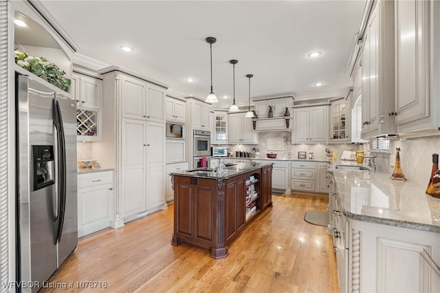 kitchen with sink, hanging light fixtures, a center island, stainless steel appliances, and light stone countertops