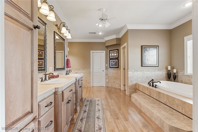 bathroom featuring hardwood / wood-style floors, tiled bath, vanity, ceiling fan, and crown molding