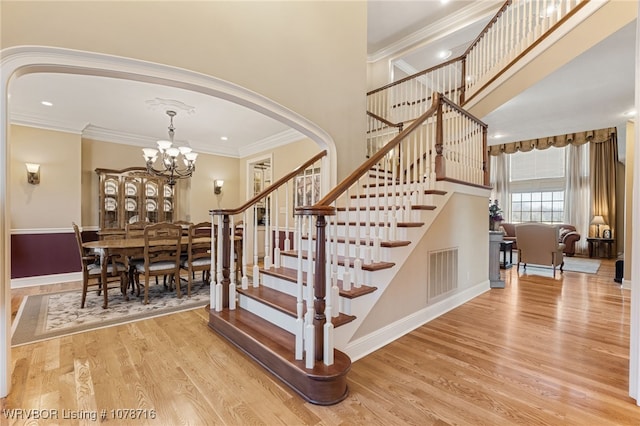 stairs featuring crown molding, a chandelier, hardwood / wood-style floors, and a high ceiling