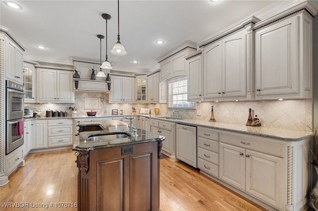 kitchen featuring decorative light fixtures, paneled dishwasher, dark stone counters, and a center island with sink