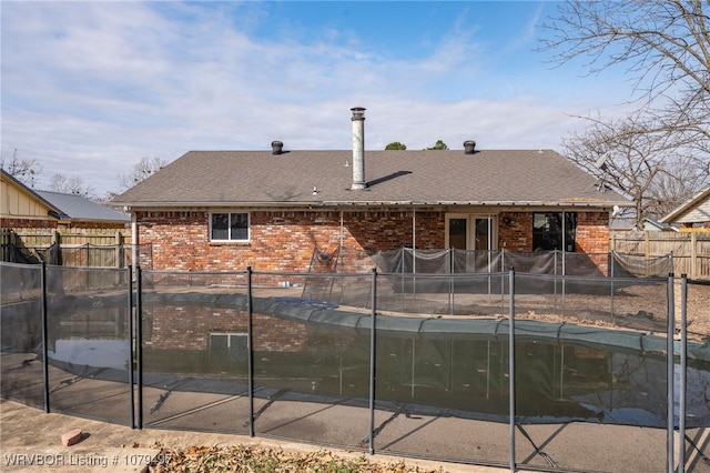 back of house with brick siding, roof with shingles, and fence