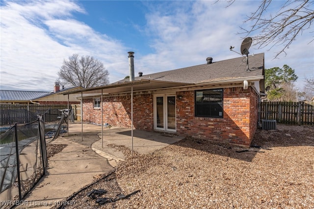 back of house with brick siding, a shingled roof, central air condition unit, a fenced backyard, and a patio area