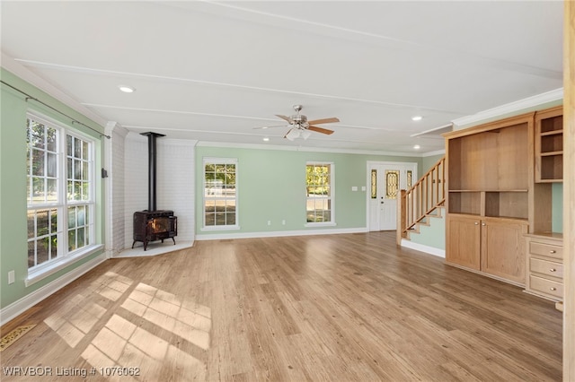 unfurnished living room with a wood stove, a wealth of natural light, light hardwood / wood-style flooring, and crown molding